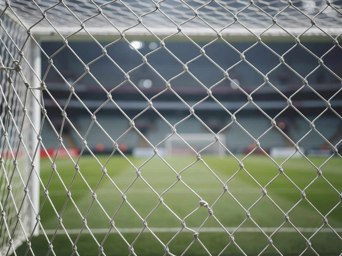 Close-up of white football goal netting with a shallow depth of field and a blurred stadium behind